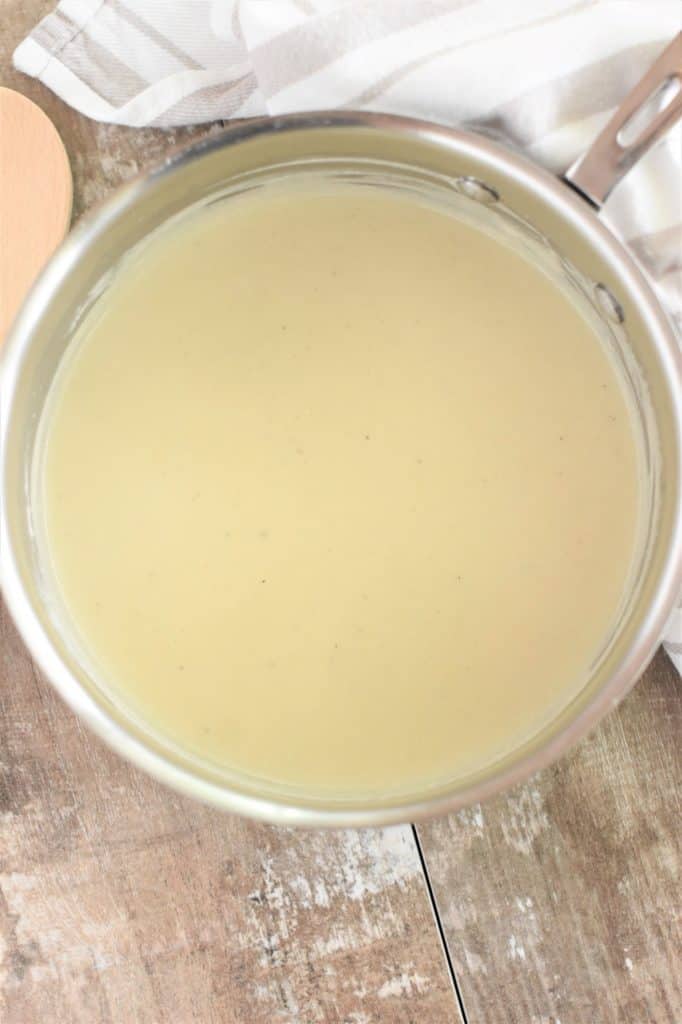 overhead of saucepan of bechamel sauce with a wooden spoon to the left of it