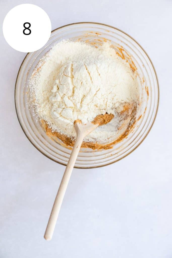 flour mixture added to mixing bowl with wooden spoon in it