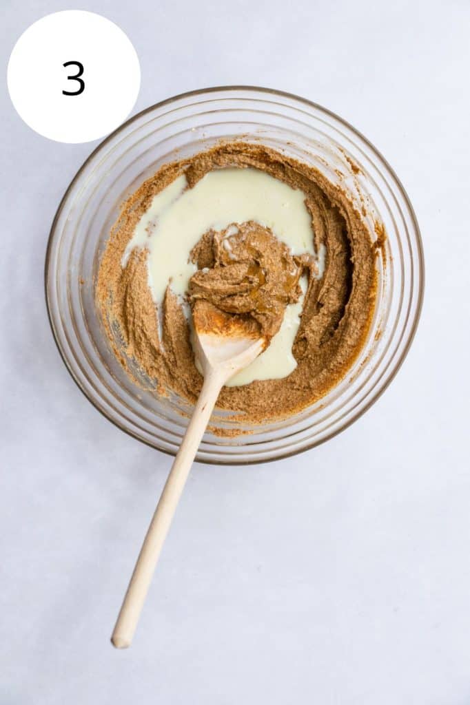 almond milk and vanilla added to pb mixture in mixing bowl with wooden spoon