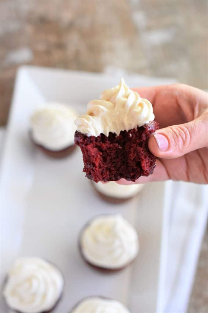 holding cupcake with frosting with a bite taken out of it