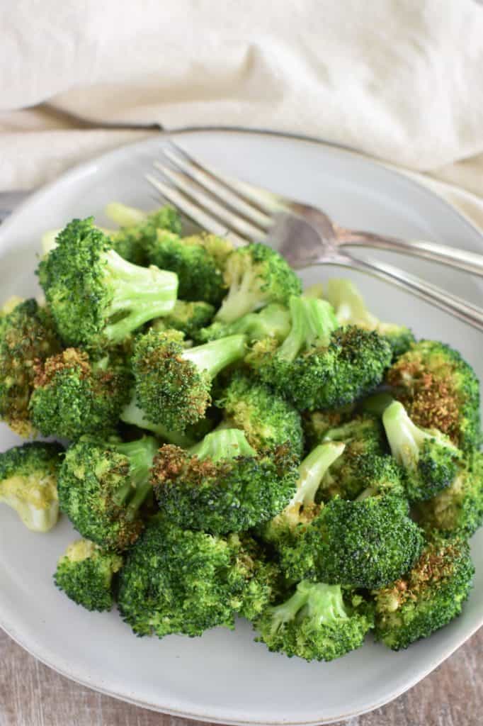 close-up overhead of broccoli on a white plate with two forks on the plate