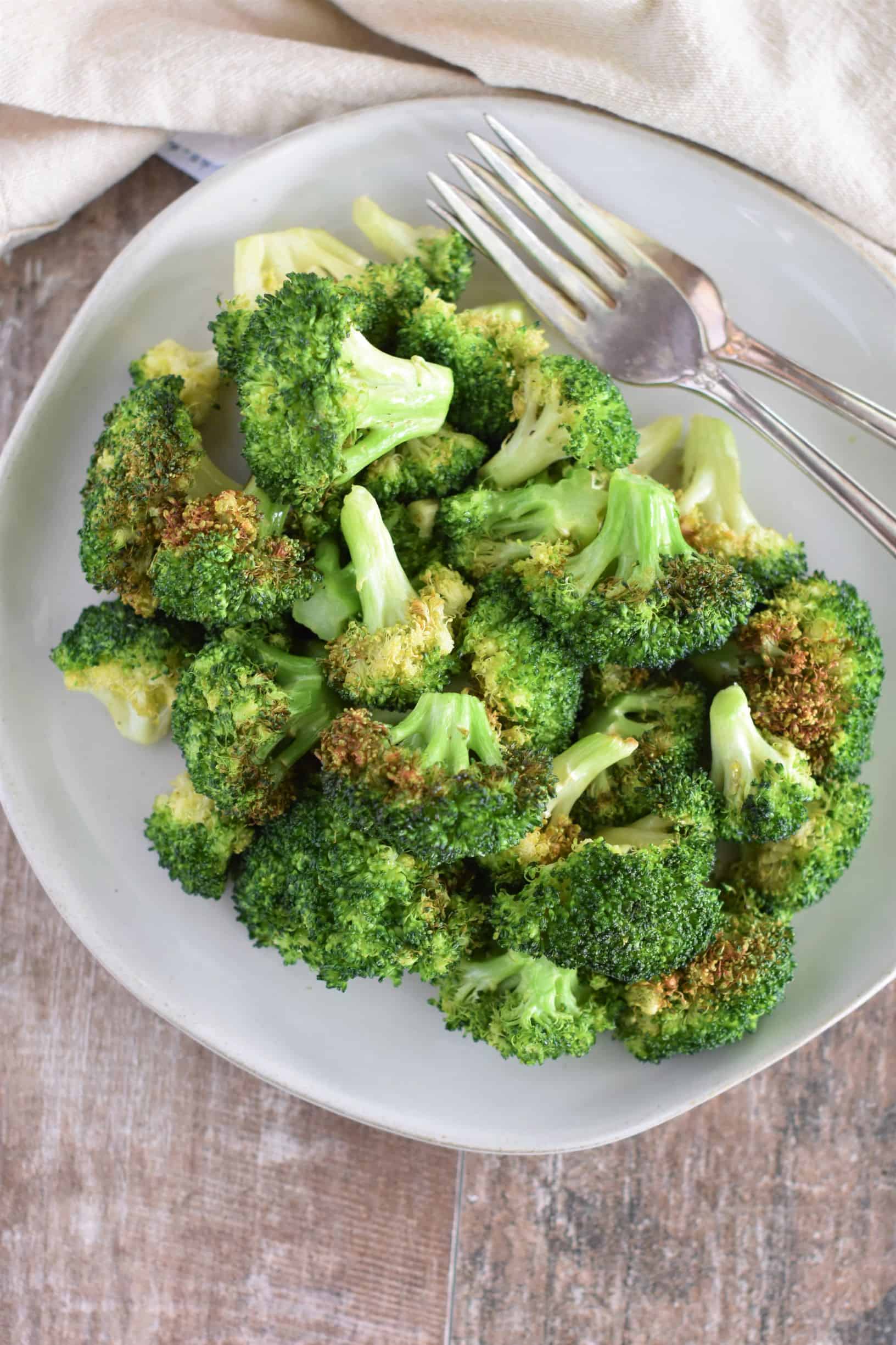 close-up of broccoli on a white plate with two forks toward the top of the plate