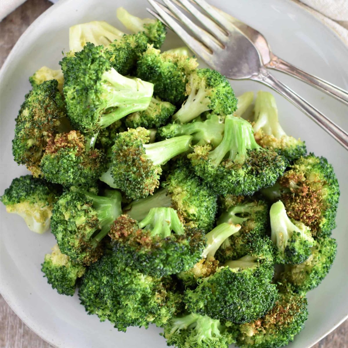 close-up overhead of broccoli on a white plate with two forks