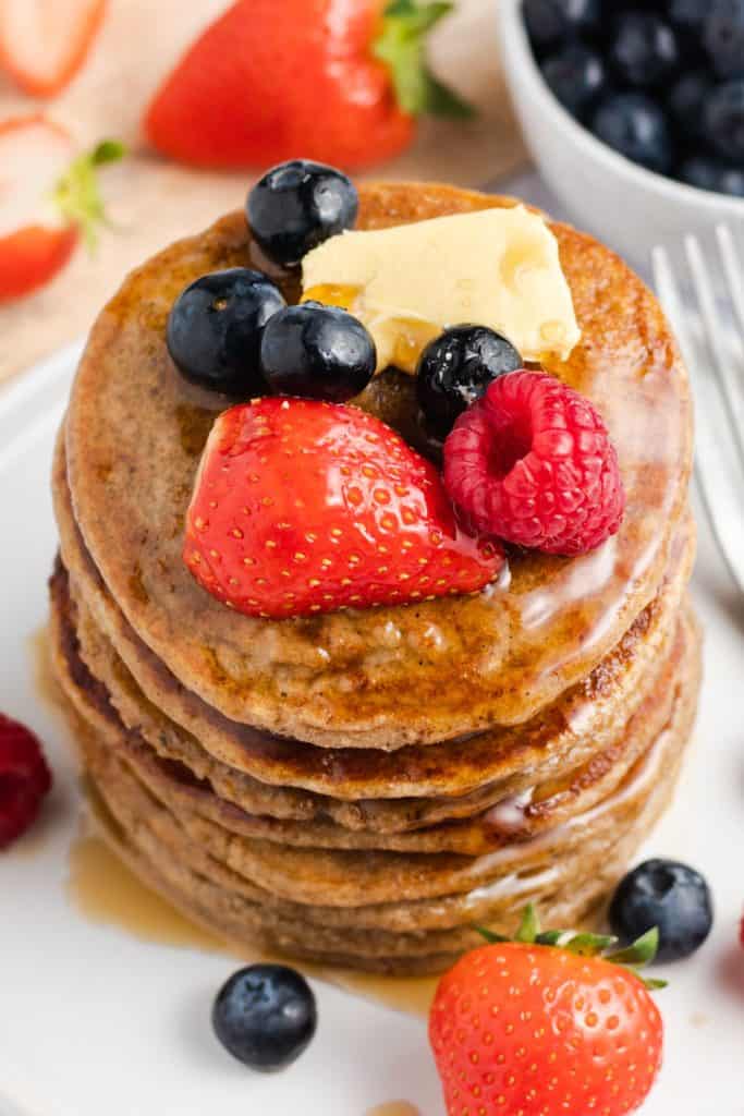 overhead view of stack of pancakes topped with vegan butter, maple syrup and fruit