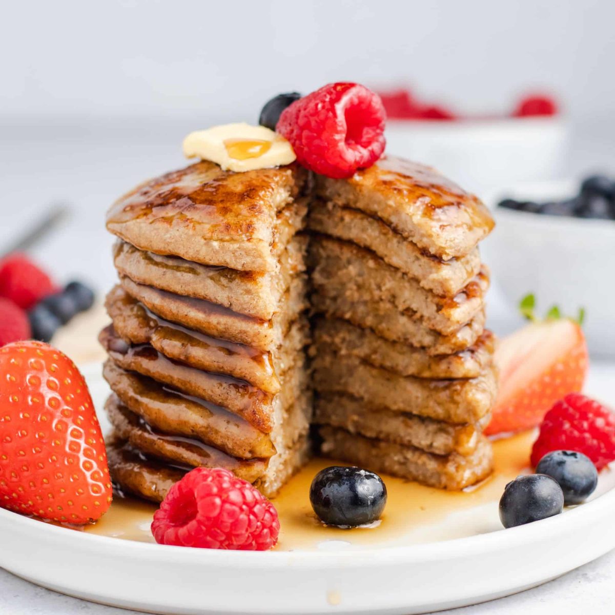 stack of pancakes with middle piece cut out and topped with vegan butter, maple syrup and fresh fruit