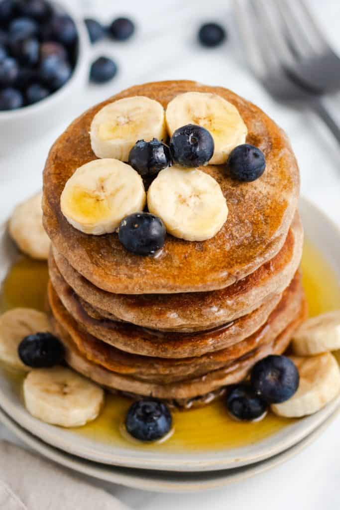 overhead of stack of pancakes with maple syrup, bananas and blueberries