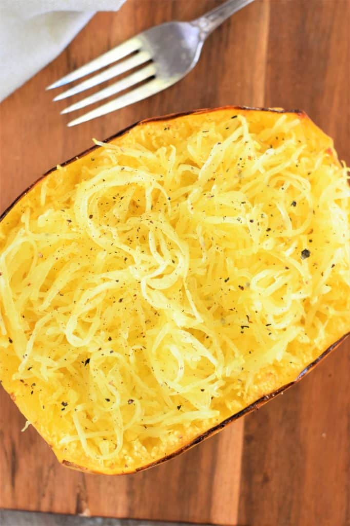 overhead of cooked spaghetti squash on a wooden board with a fork on the board