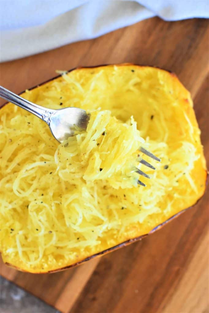 forkful of spaghetti squash strands hovering over one of the halves