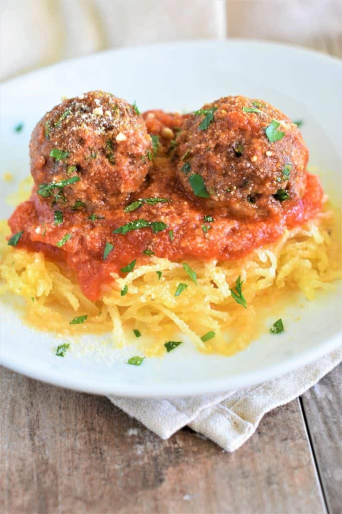spaghetti squash on a white plate topped with sauce, vegan meatballs and vegan Parmesan