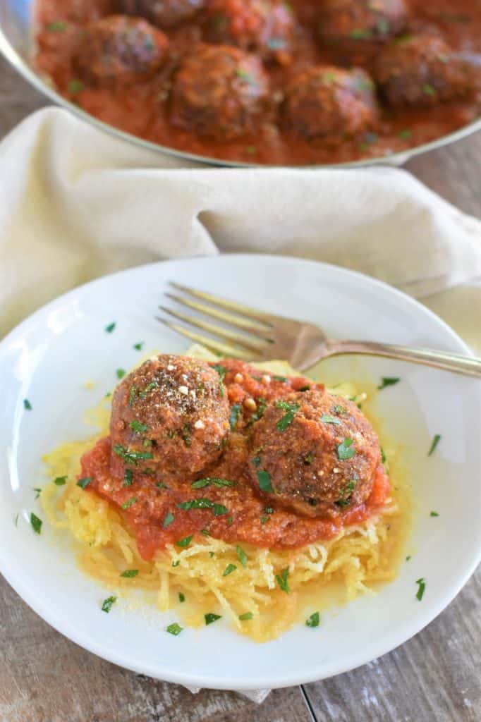 meatballs on top of spaghetti squash on a white plate with rest behind it in skillet