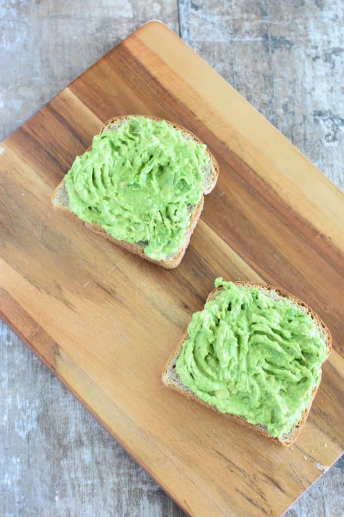 two slices of toast on wooden board with mashed avocado