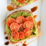 close-up of slice of tomato avocado toast on white serving dish with part of another one behind it