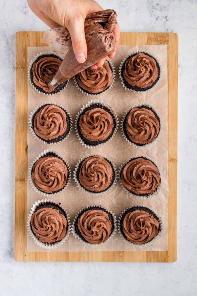 icing the cupcakes on parchment on a wooden board