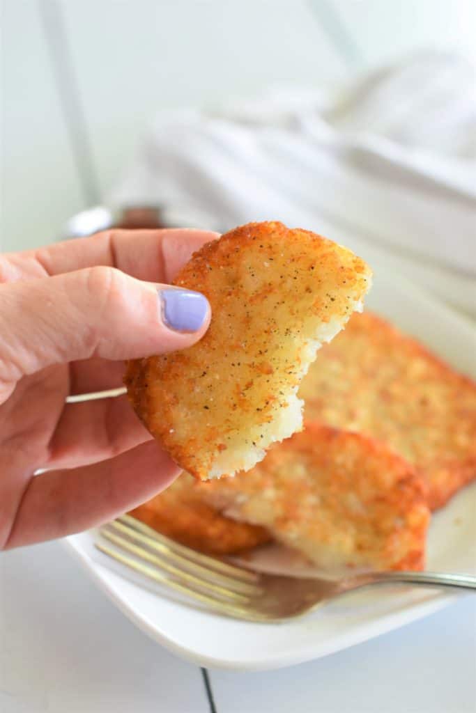 holding up a piece of a hash brown patty with salt and pepper on it