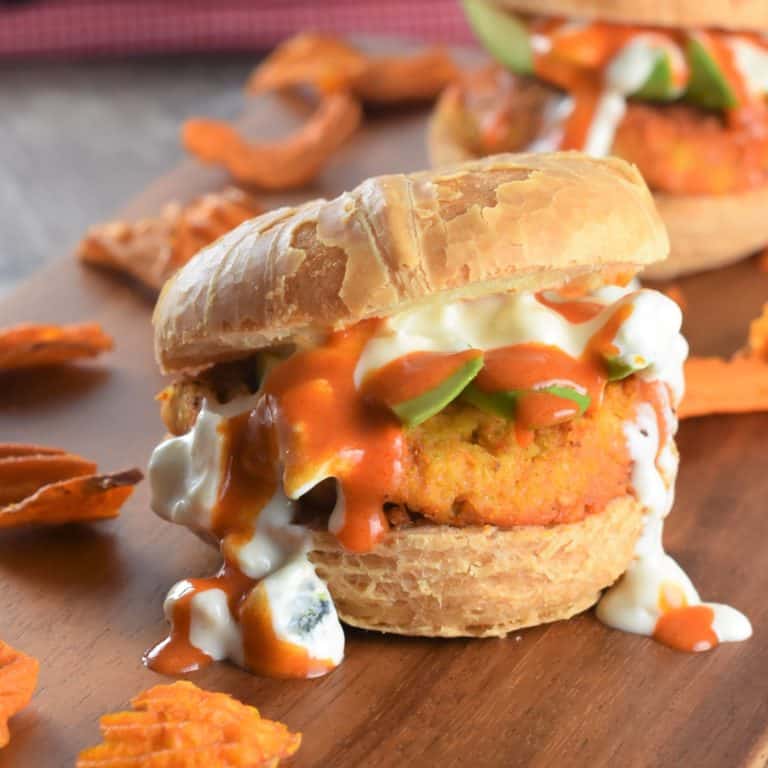 close-up of burger with avocado, Buffalo sauce and blue cheese dressing on wooden board with sweet potato chips around and another one in the background
