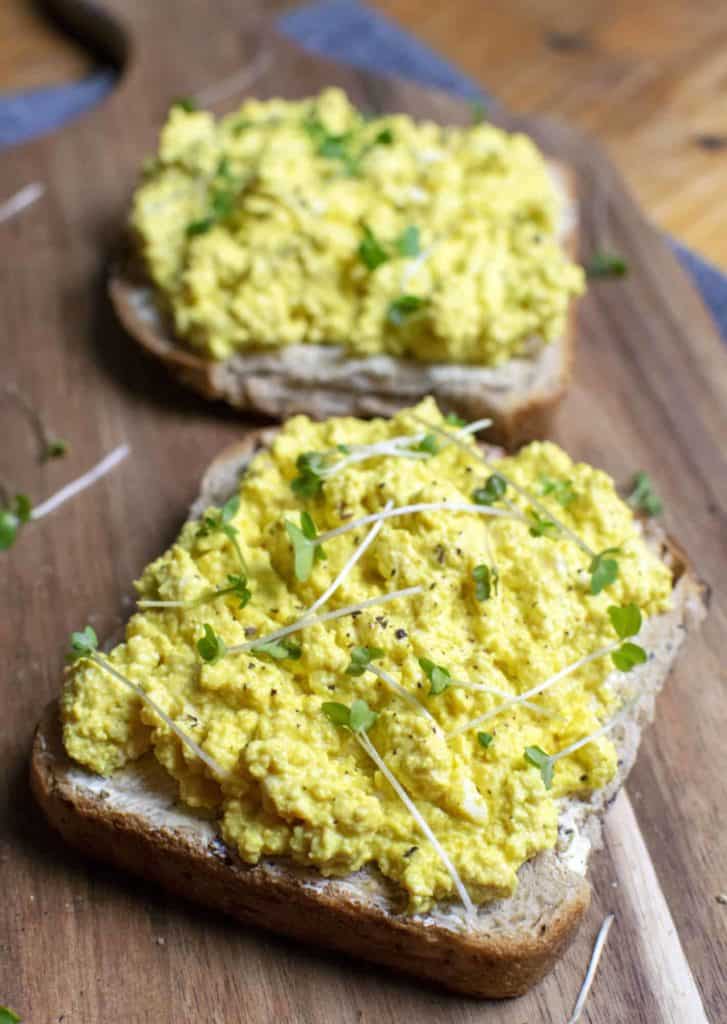 open-faced vegan egg mayo sandwiches on wooden board garnished with microgreens