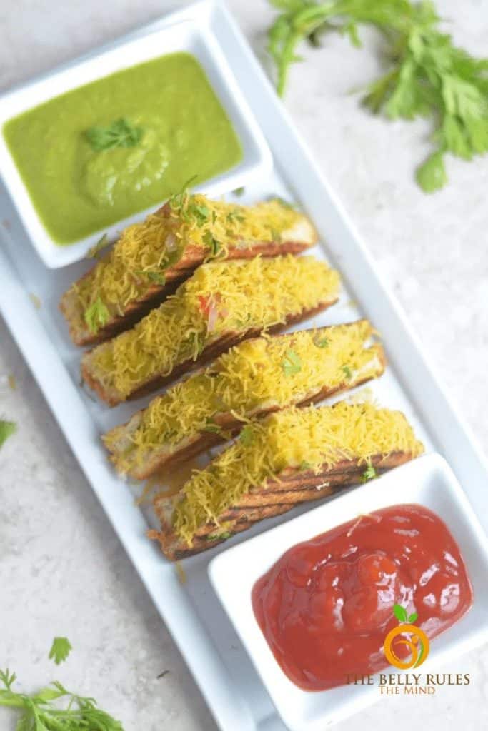 masala vegetable sandwiches on a white serving dish with dipping sauces