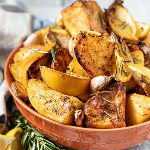roasted potatoes in orange bowl with rosemary and lemon wedges