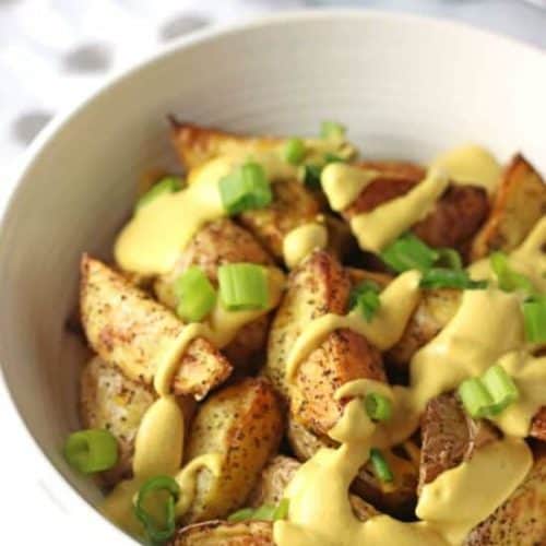 vegan cheesy potato wedges in white bowl topped with scallions