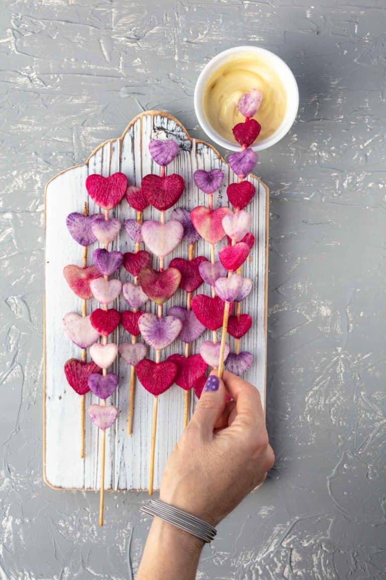 radish heart wands on white wooden board with hand taking one and dipping it into dipping sauce