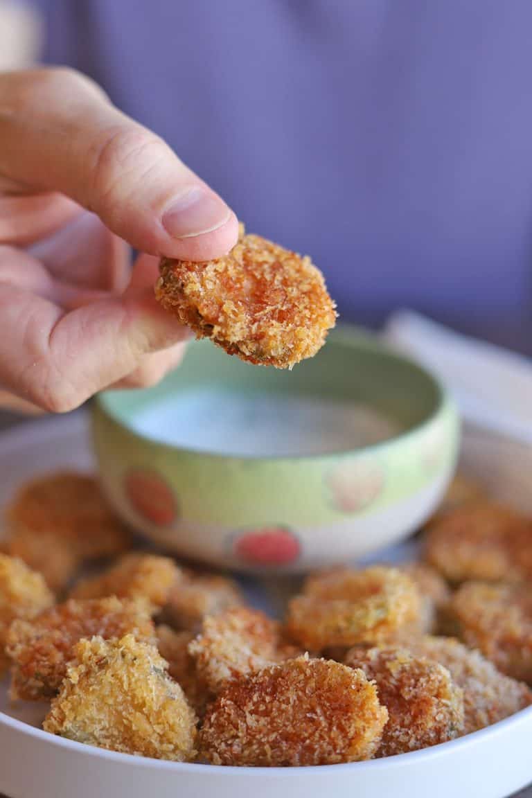 holding an air fried pickle up with other ones in serving bowl