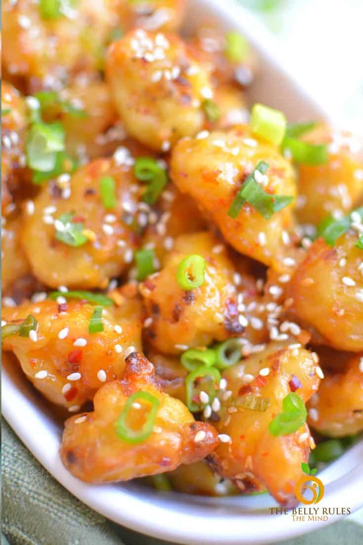 vegan orange cauliflower in white bowl topped with sesame seeds and scallions