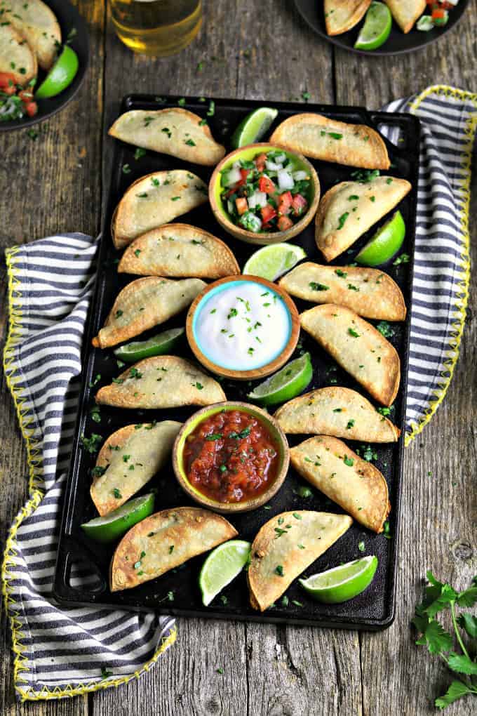 potato tacos on serving tray with salsa, pico de gallo and vegan sour cream serving dishes
