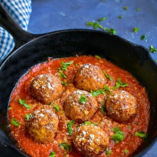 cauliflower meatballs in a cast iron skillet with sauce, basil and vegan Parmesan