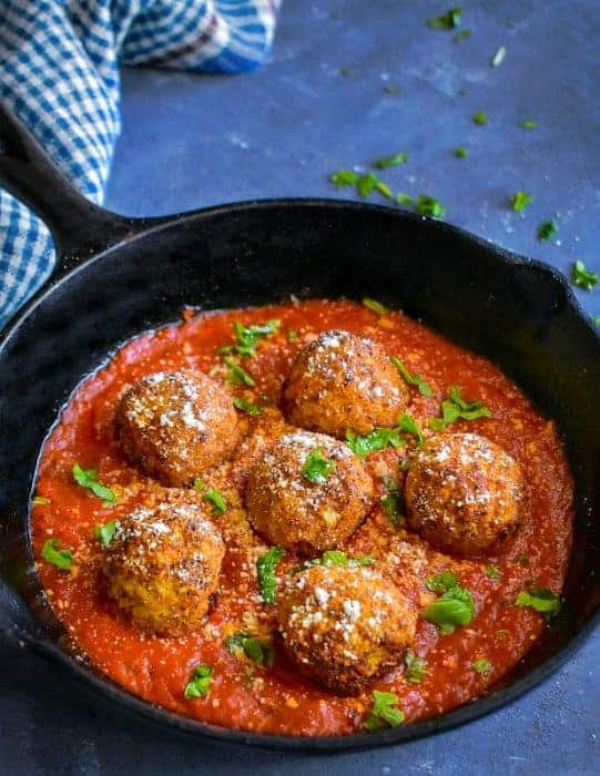 cauliflower meatballs in a cast iron skillet with sauce, basil and vegan Parmesan
