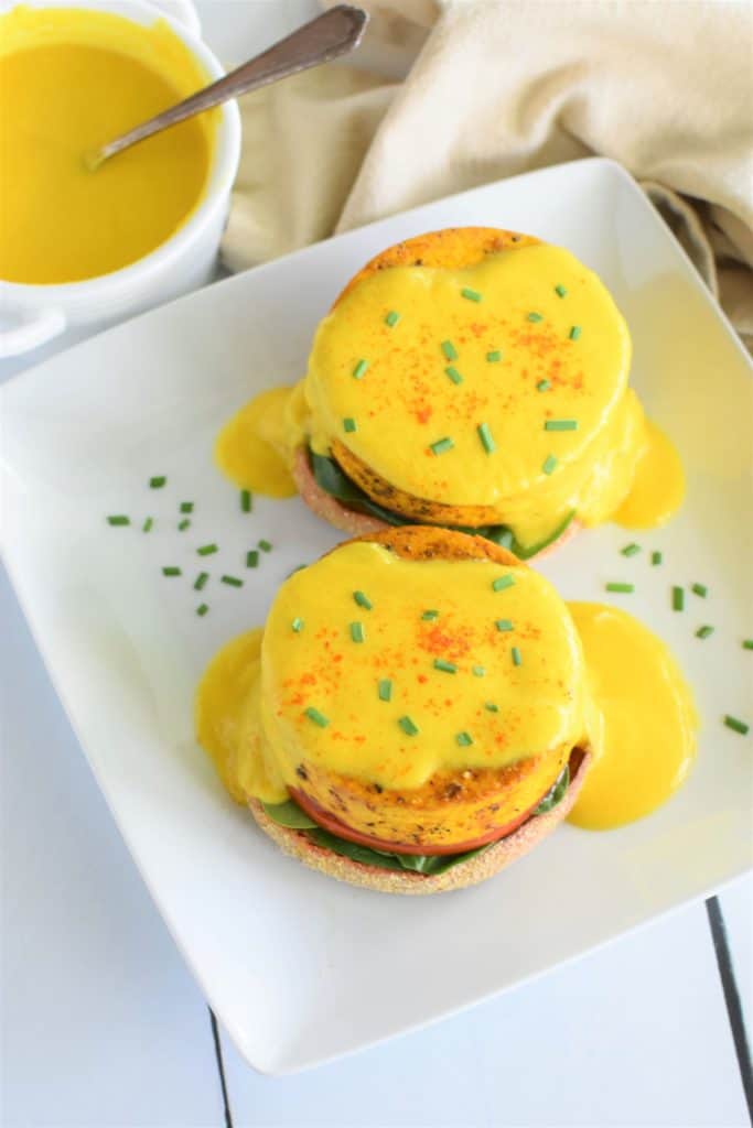 overhead view of two tofu Benedicts on white plate with side of hollandaise sauce with a spoon in it