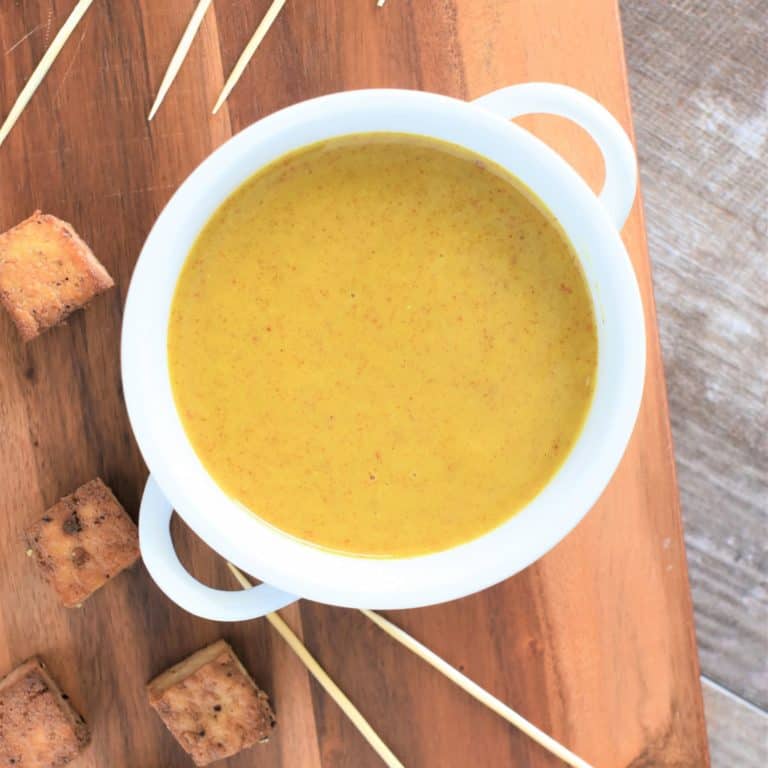 A white bowl of honey mustard is topped with cubes of tofu and skewers placed around it.
