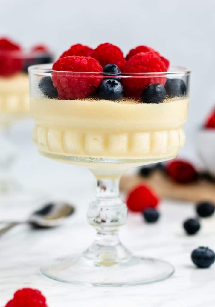 front view of one serving of pudding in a glass container topped with raspberries and blueberries
