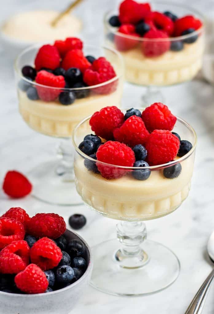 three servings of pudding in glass containers topped with berries and a cup of extra berries
