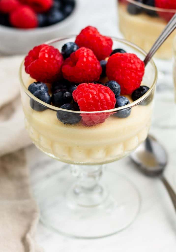 close-up of serving of pudding in glass container topped with berries with a spoon in it