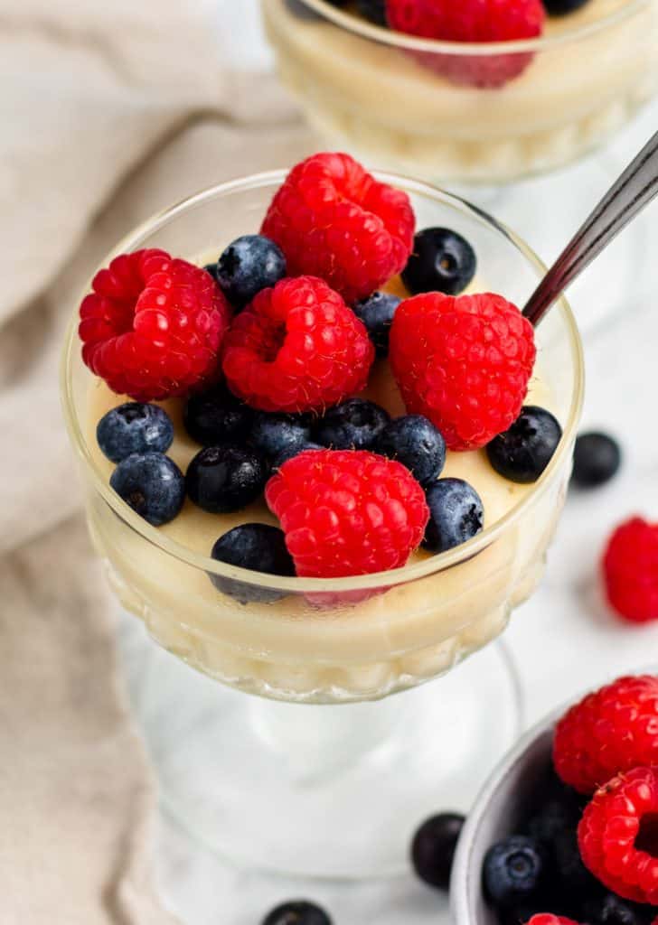 overhead of serving of pudding topped with berries with spoon in it and another one partially in the background with some extra berries around