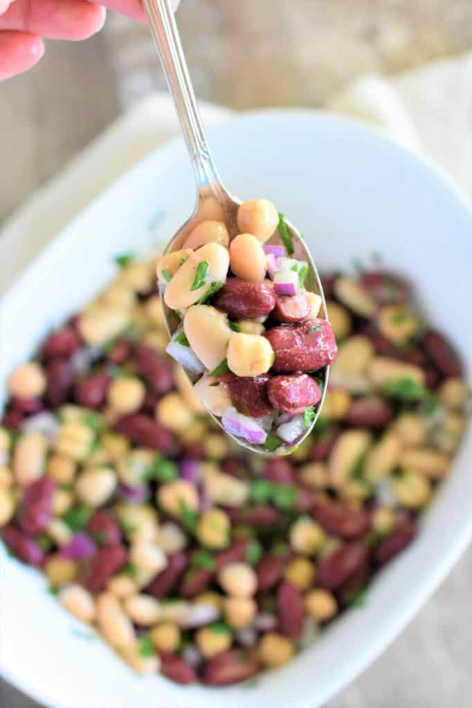 holding a spoonful of bean salad over the rest of it in white mixing bowl