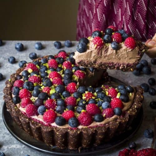 holding up slice of vegan chocolate mousse pie topped with berries over the rest of it