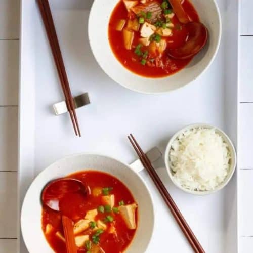 overhead of two bowls of Vegan Kimchi Soup with chopsticks and rice on the side