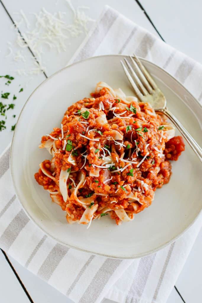 overhead of tagliatelle mixed with red lentil bolognese garnished with parsley and Parmesan and with a fork on the plate