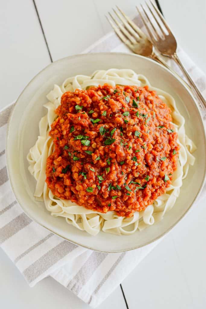 overhead of pasta with sauce on plate garnished with parsley and with two forks to the right