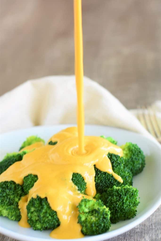 stream of cheese sauce being poured onto a plate of broccoli
