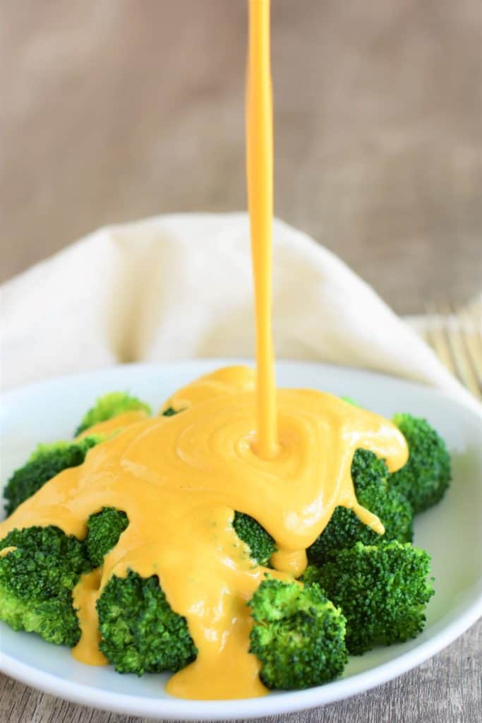 vegan cheese sauce being poured onto broccoli on a white plate