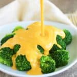 cheese sauce being poured onto plate of broccoli