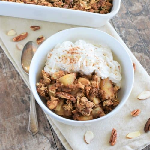 overhead of pear crisp with non-dairy whipped topping and some nuts around it and a spoon next to it