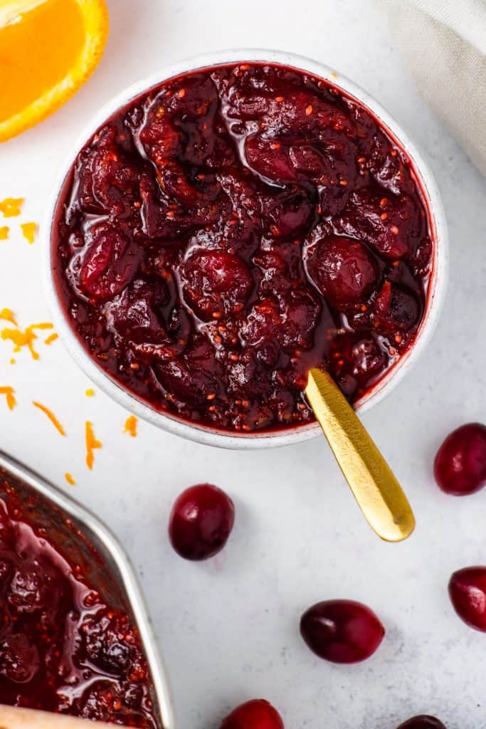 far overhead of cranberry sauce in serving bowl with spoon in it and some cranberries scattered around