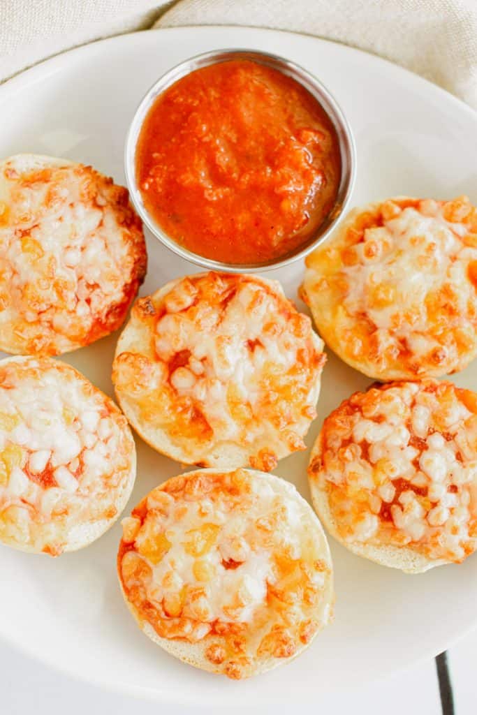 close-up overhead of bagel bites on a white plate with cup of marinara sauce