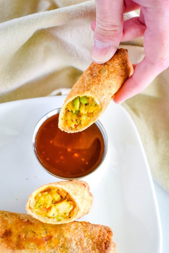 holding an open egg roll over dipping sauce before dipping.