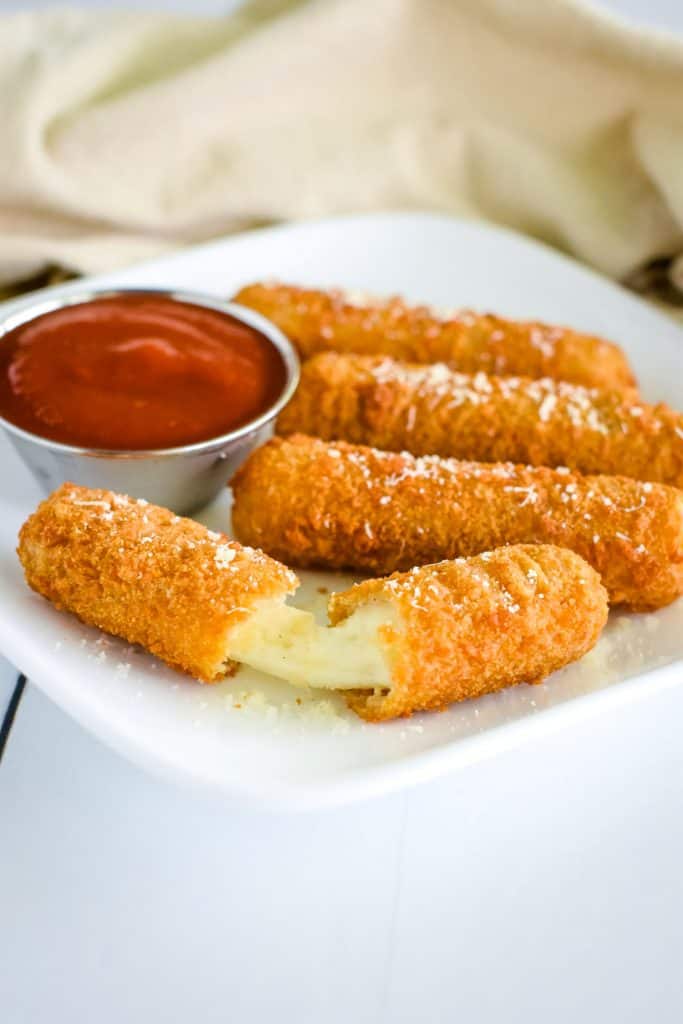 mozzarella sticks on a plate with the one in the front opened to show the cheese