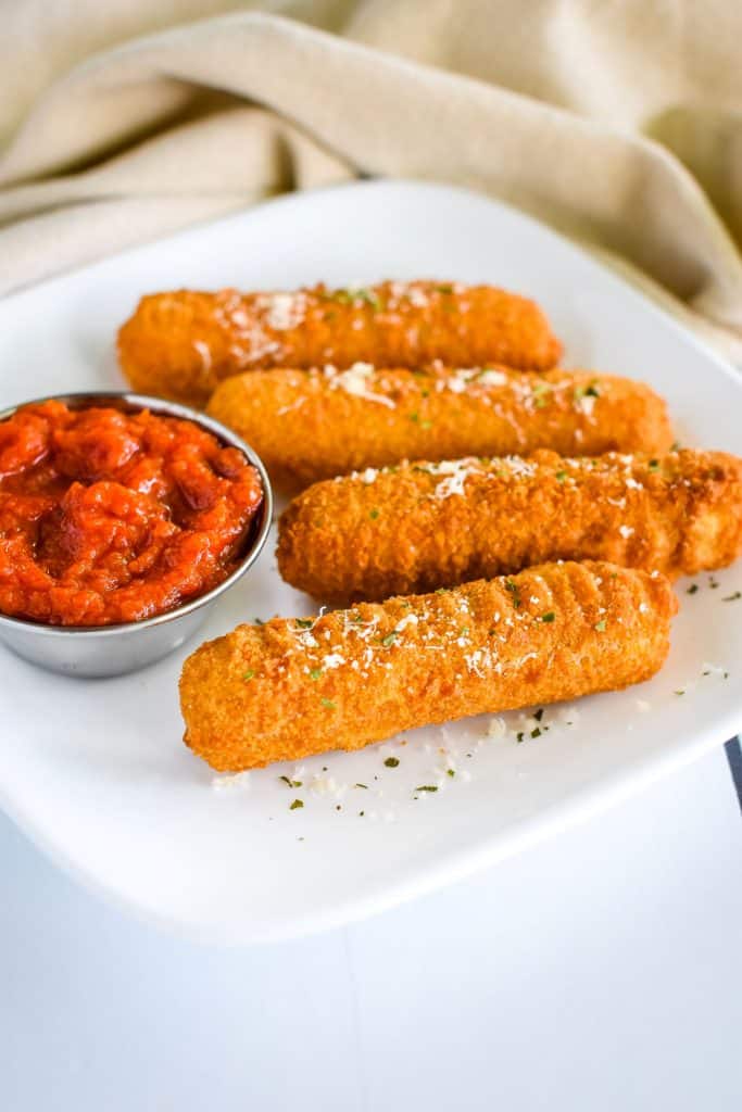 front view of mozzarella sticks on white plate with marinara sauce and garnished with Parmesan and parsley
