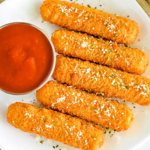 close-up overhead of plate of 5 mozzarella sticks with tomato sauce on the side